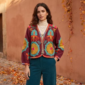 Mujer de pie con chaqueta bordada en color berenjena con bordados en turquesa, naranja y rosa Modamiomio