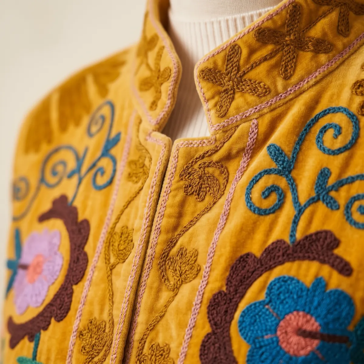 Detalle de cuello mao y cierre frontal de chaqueta de terciopelo mostaza con delicados bordados florales en tonos azules y marrones Miomio